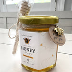 Jar of honey with a gold lid and bee-themed label on a white surface.