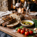 Wooden cutting board with sliced bread, tomatoes, and a bowl of oil and herbs on a rustic wooden table.